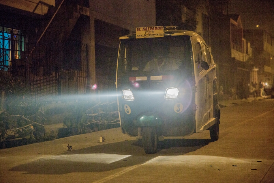 The lights of a mototaxi (three wheeler bike with driver and 2/3 passengers) cuts through the smoke-filled streets of Villa El Salvador, Lima